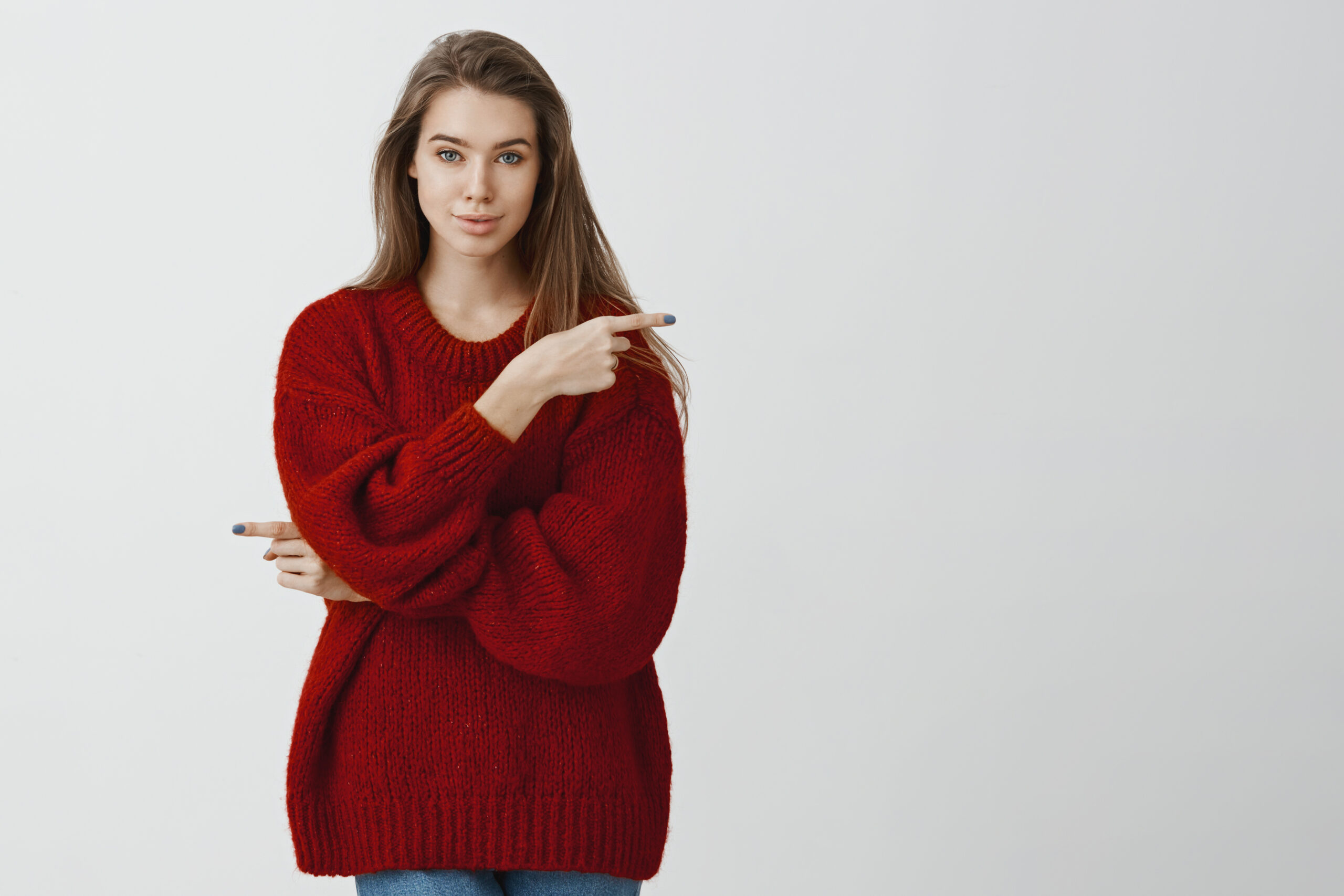 Woman gives us opportunity to chose way in life. Confident feminine european girl in stylish red loose sweater, pointing in different directions, excepting every possibility over gray background